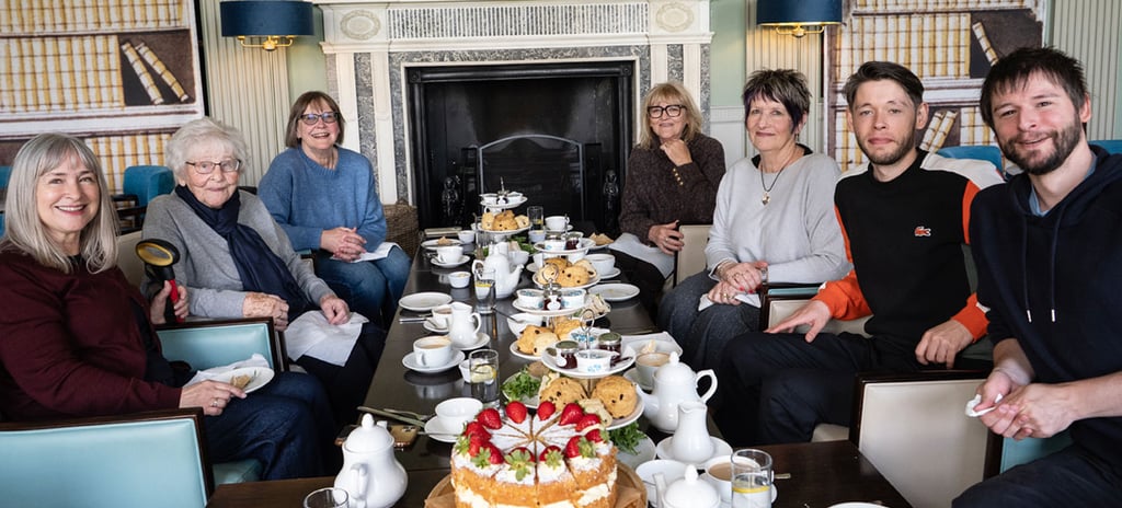 Family gathered around a table with afternoon tea and cake to celebrate Joan Tait's 100th birthday at Attingham, Shropshire.
