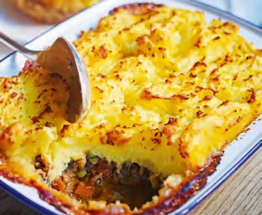 A golden mushroom and lentil cottage pie with a metal serving spoon resting in the dish.