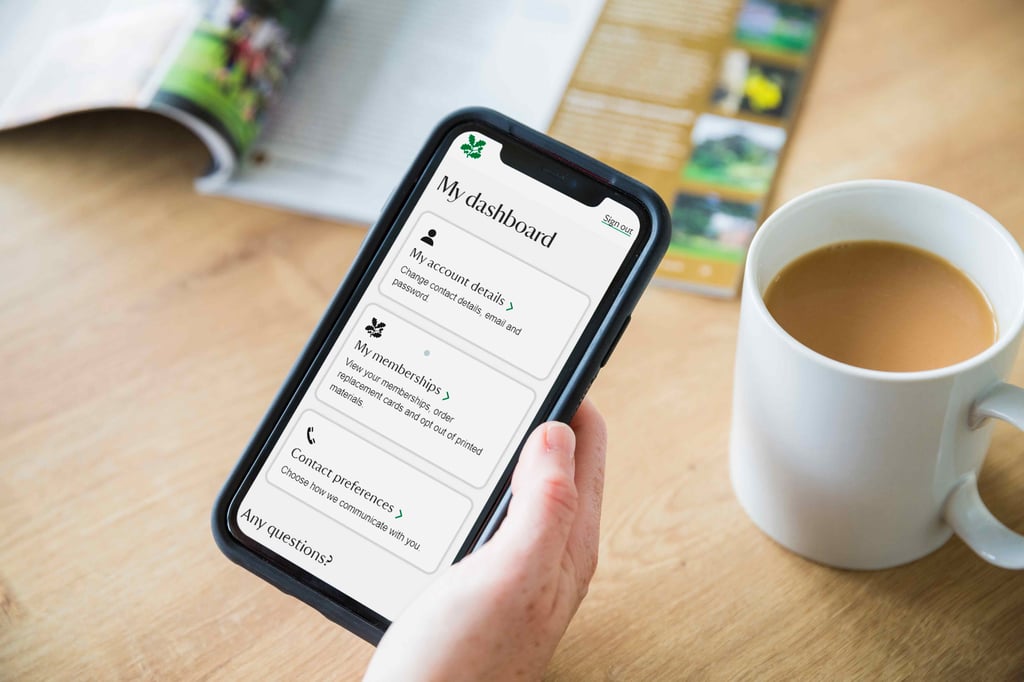 Person using the National Trust app on a mobile phone beside a cup of tea.