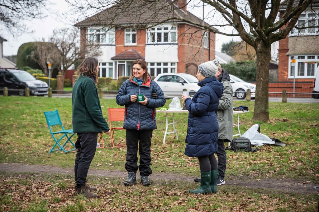 Group of people chatting in a residential park while holding hot drinks.