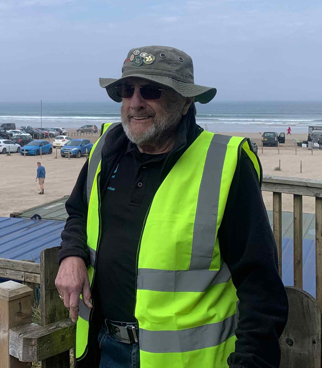 Long-term dune volunteer William, known as "BT", wearing a high-visibility vest while looking across the dunes at Portstewart Strand, County Londonderry at a beach cafe.