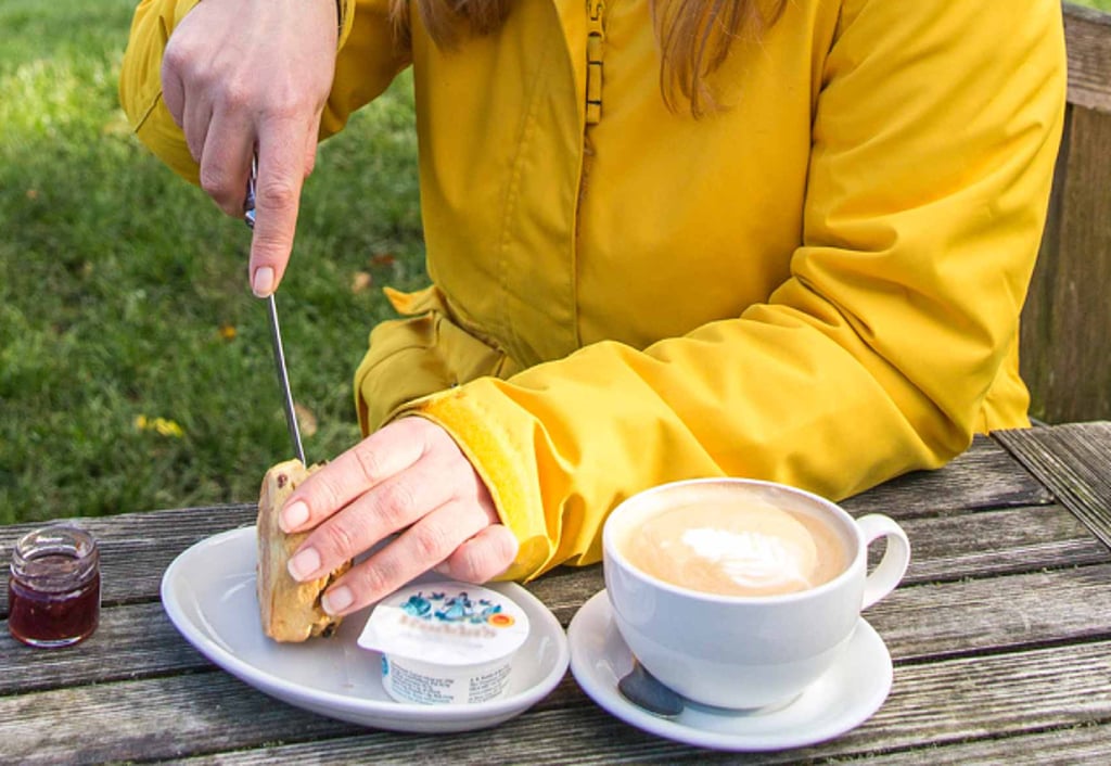 Person cutting into scone with clotted tea and a latte. 
