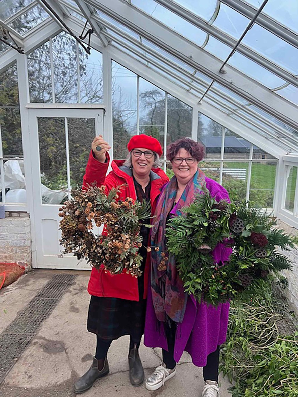 Sarah and Anne holding large Christmas wreaths inside a greenhouse.
