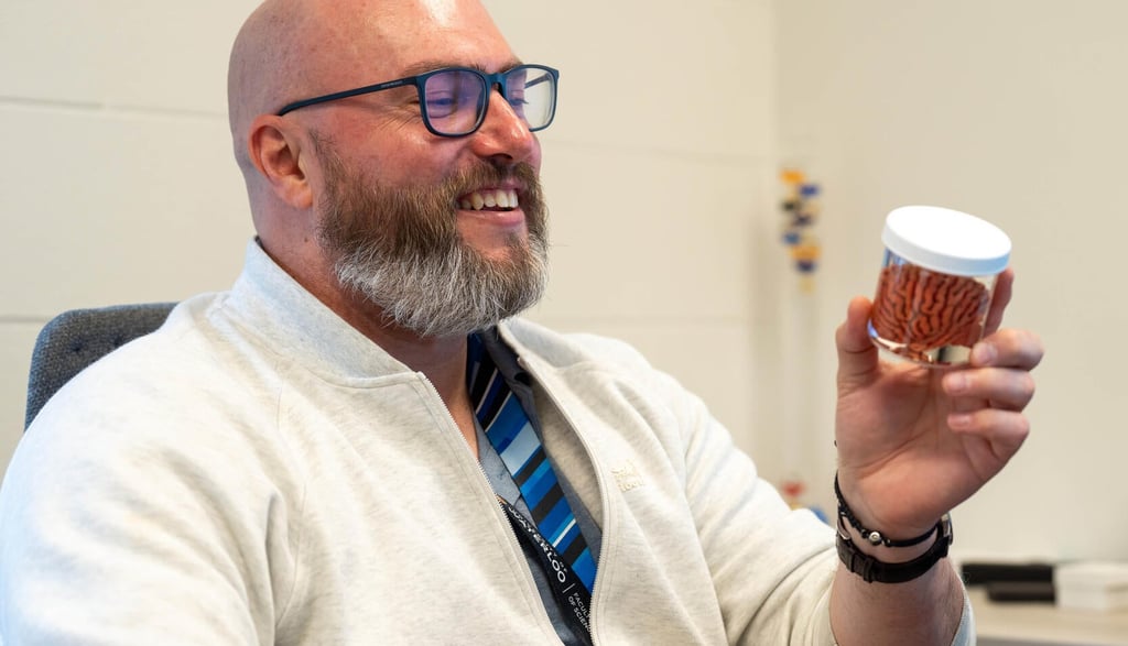 Travis Craddock examines a miniature model of a brain in a jar while seated at his desk.